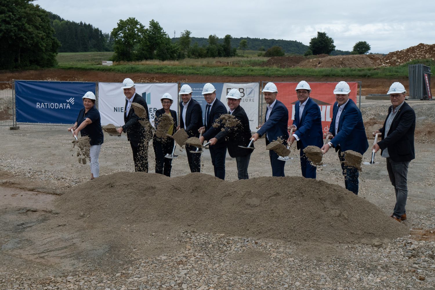 Zehn Personen, die für das Neubauprojekt der Ratiodata in Velburg verantwortlich sind sowie Verantwortliche der Stadt Velburg beim symbolische Spatenstich mit Schaufeln vor einem Erdhaufen.