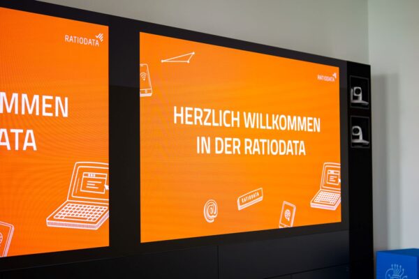 Orangener Screen begrüßt die Azubis mit "Herzlich Willkommen in der Ratiodata"