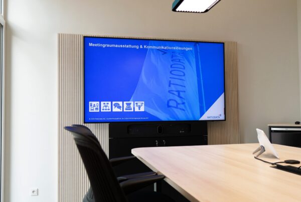 Kleiner Meetingraum mit einem Tisch und Stühlen uns einem Display mit einer Präsentation zu Medientechnikausstattung & Kommunikationslösungen